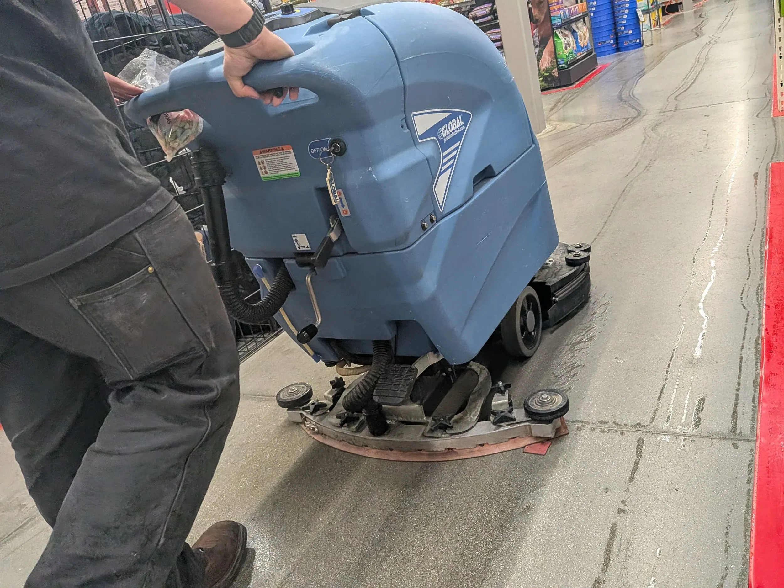 A ride-on scrubber cleaning the polished concrete aisles of a retail store.